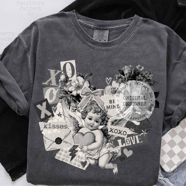 May include: Dark gray sweatshirt with a vintage-style graphic featuring a cherub holding a heart, surrounded by floral elements, the words "XOXO", "LOVE", and "kisses". The text "BE MINE" and "ORIGINAL DESIGNER" are also present.