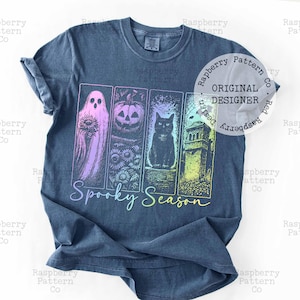Peut inclure: Un t-shirt bleu fonc&eacute; avec une impression graphique de quatre panneaux verticaux contenant un fant&ocirc;me avec un tournesol, une citrouille, un chat noir et une tour hant&eacute;e. Le texte Spooky Season est imprim&eacute; en d&eacute;grad&eacute; sous les panneaux.