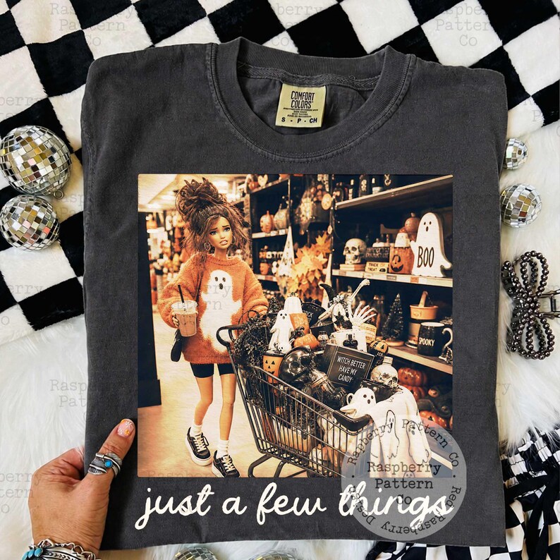 May include: A charcoal gray t-shirt featuring a graphic print of a doll in an orange ghost sweater pushing a shopping cart filled with Halloween decor. The text "WITCH BETTER HAVE MY CANDY" and "just a few things" is printed on the shirt.