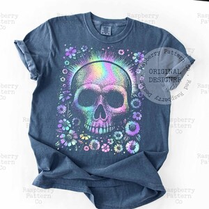 Pu&ograve; includere: T-shirt blu con un design colorato a teschio circondato da fiori. Il teschio ha un effetto iridescente arcobaleno e i fiori sono in tonalit&agrave; viola, blu e giallo. La maglietta ha un girocollo e maniche corte.