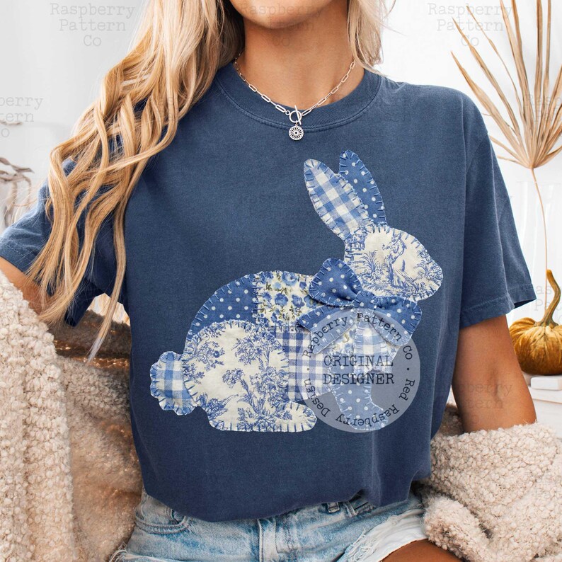 May include: Navy blue t-shirt featuring a patchwork bunny design. The bunny is composed of various blue and white patterned fabrics, including polka dots, gingham, and floral prints. The text "ORIGINAL DESIGNER" is printed on the shirt.