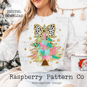 May include: A white sweatshirt with a colorful Christmas tree design. The tree is decorated with a black and white polka dot bow and gold glitter. The text "Raspberry Pattern Co" is printed on the bottom of the sweatshirt.