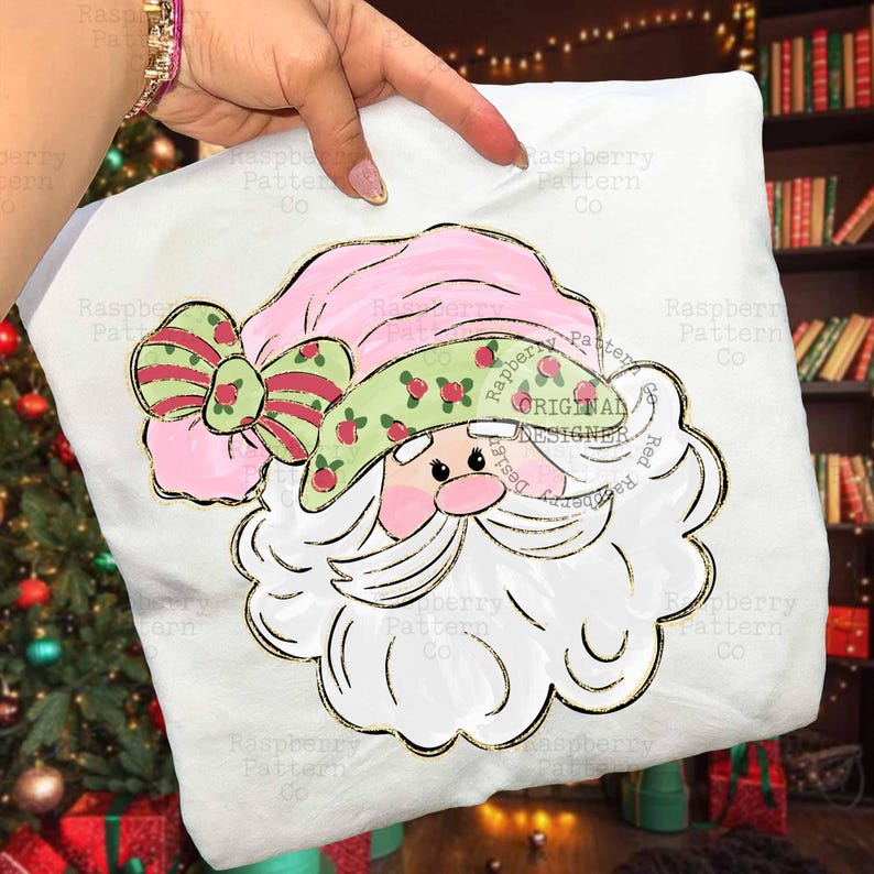 May include: A white pillow with a Santa Claus design. The Santa has a pink hat and a green hatband with red berries. A large bow with red stripes and green accents is on the hat. The design is outlined in gold.