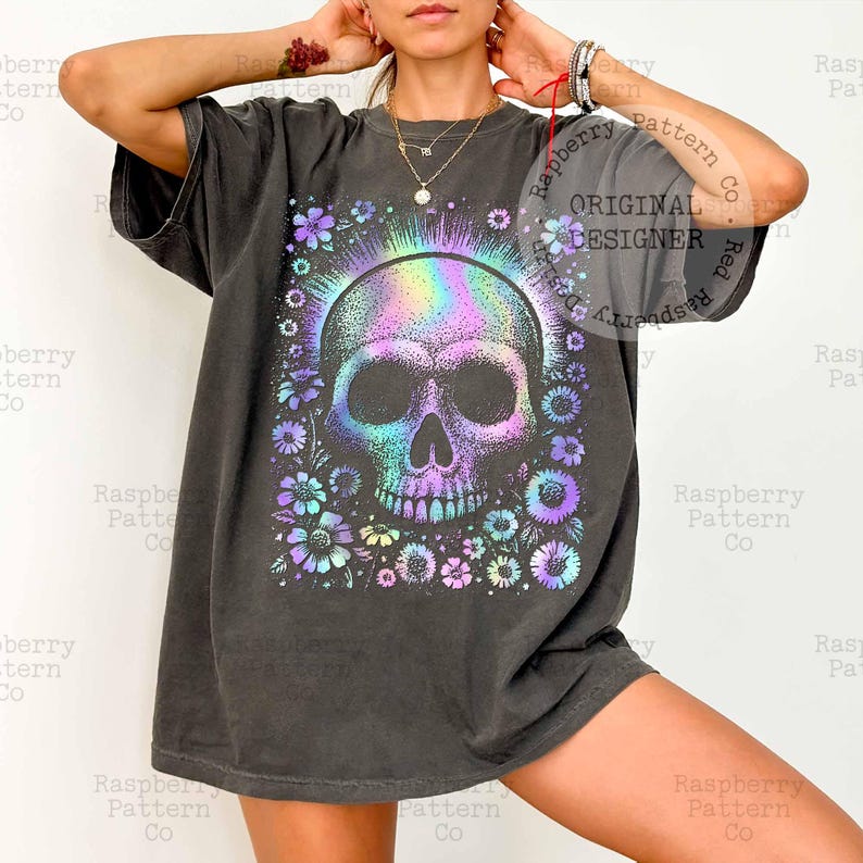 Pu&ograve; includere: T-shirt grigio scuro con un design a teschio colorato circondato da fiori. Il teschio ha un effetto iridescente arcobaleno. La maglietta ha la scritta "ORIGINAL DESIGNER" in alto a destra.