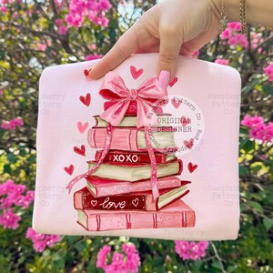 May include: A light pink tote bag featuring a stack of books with a pink bow and ribbon. The books are in shades of pink and red, with the words "XOXO" and "love" on them. Red hearts are scattered around the books.