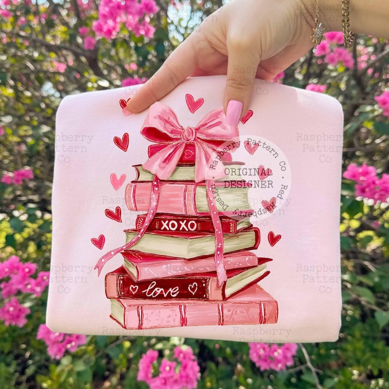 May include: A light pink tote bag featuring a stack of books with a pink bow and ribbon. The books are in shades of pink and red, with the words "XOXO" and "love" on them. Red hearts are scattered around the books.