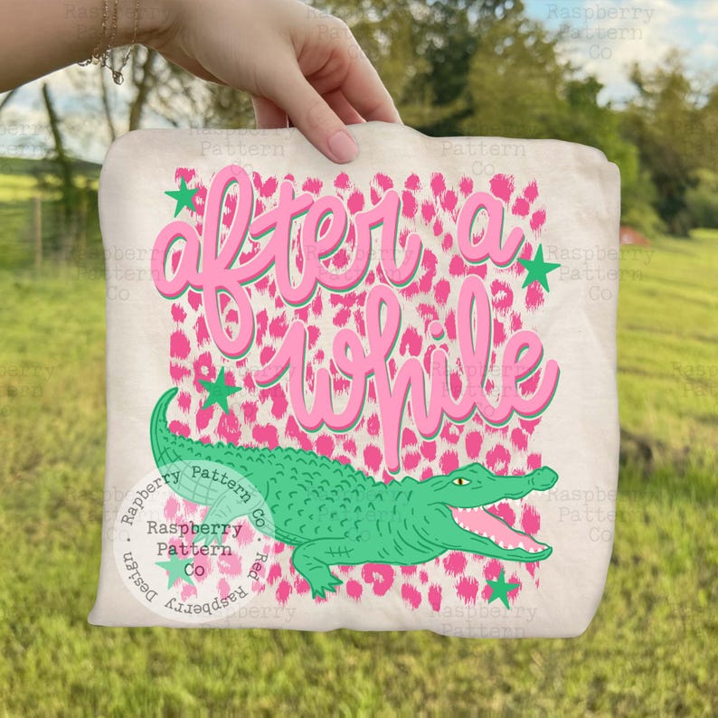 May include: A beige tote bag with the text "after a while" in pink script, a green alligator, and pink leopard print background. Green star accents are scattered around the text and alligator.