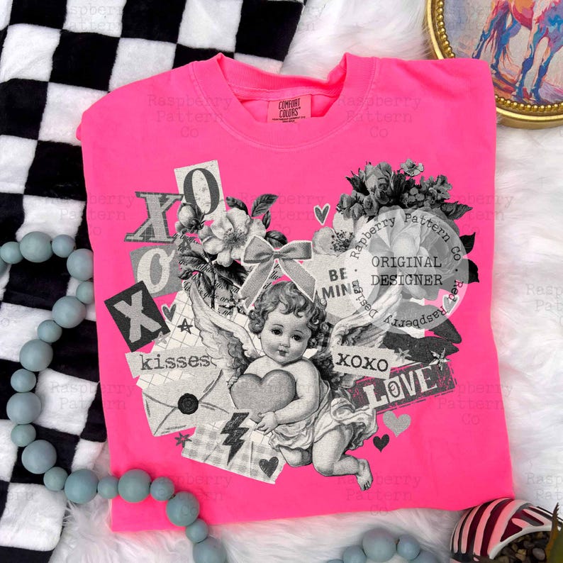 May include: Bright pink crew neck t-shirt with a collage design. The design includes an angel holding a heart, flowers, and the words "XOXO", "kisses", and "LOVE". The shirt is made of a soft material.