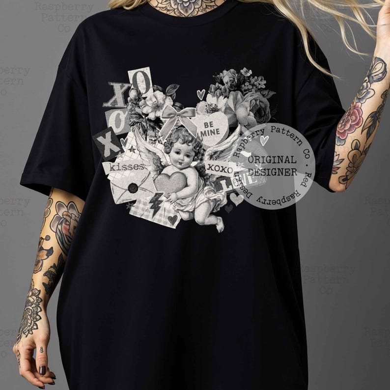 May include: Black t-shirt featuring a vintage-style graphic with an angel holding a heart, surrounded by floral elements, the words "BE MINE", and "XOXO". The design includes the text "kisses" and "ORIGINAL DESIGNER".
