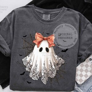 K&ouml;nnte beinhalten: Dunkelgraues Sweatshirt mit einem wei&szlig;en Geist-Design, roter Schleife, schwarzen Augen und Spitzendetails. Ein Spinnennetz und Flederm&auml;use umgeben den Geist. Text: "Raspberry Pattern Co" und "Original Designer".