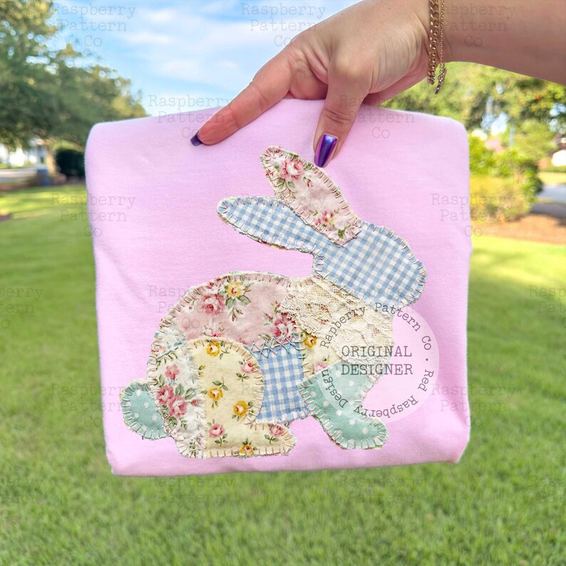 May include: A light pink t-shirt featuring a patchwork bunny design. The bunny is made of floral and gingham fabrics, with lace accents. The design includes the text "ORIGINAL DESIGNER".