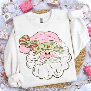 May include: White sweatshirt featuring a Santa Claus design. The Santa Claus graphic has a pink hat and bow, a green hat with red accents, and a white beard. The words "ORIGINAL DESIGNER" are in a circle.