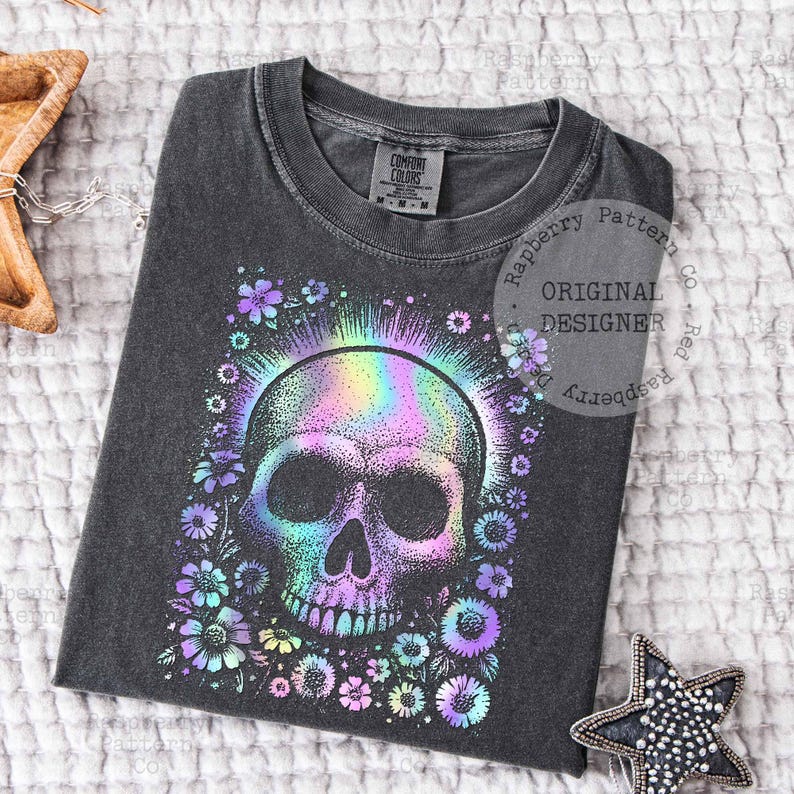Pu&ograve; includere: T-shirt grigio scuro con un design a teschio colorato circondato da fiori. Il teschio ha un effetto olografico arcobaleno. La maglietta &egrave; del marchio Comfort Colors. Il design include il testo "Original Designer".