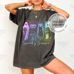 Peut inclure: Un t-shirt gris anthracite &agrave; manches courtes avec une impression graphique compos&eacute;e de quatre panneaux verticaux repr&eacute;sentant un fant&ocirc;me, une citrouille, un chat noir et une pierre tombale, avec le texte Spooky Season en &eacute;criture cursive.