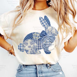 May include: Cream-colored t-shirt featuring a patchwork bunny design in shades of blue. The bunny is composed of various patterned fabrics, including floral, polka dot, and gingham. The text "ORIGINAL DESIGNER" is visible on the design.
