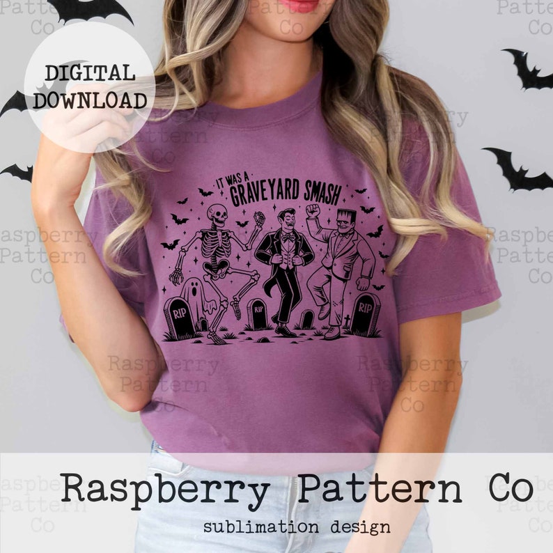 Puede incluir: Una camiseta morada con un dise&ntilde;o gr&aacute;fico negro de un esqueleto, un vampiro y un monstruo de Frankenstein bailando. El texto en la camiseta dice "It was a Graveyard Smash".