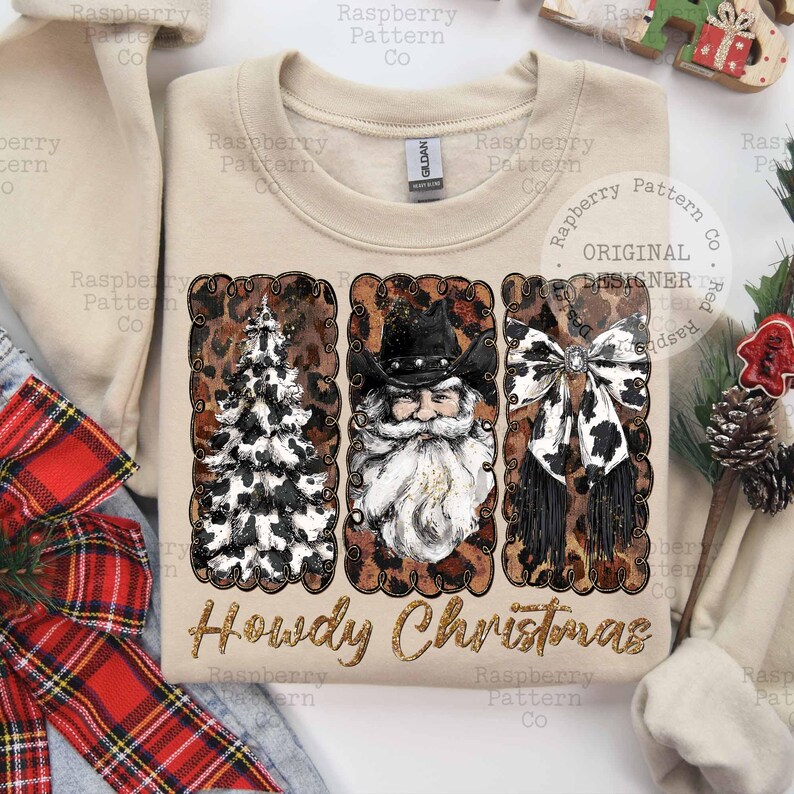 May include: Beige sweatshirt with a festive design. The design includes a Christmas tree, Santa Claus wearing a cowboy hat, and a bow, all with a cowhide pattern. The text "Howdy Christmas" is below the images.