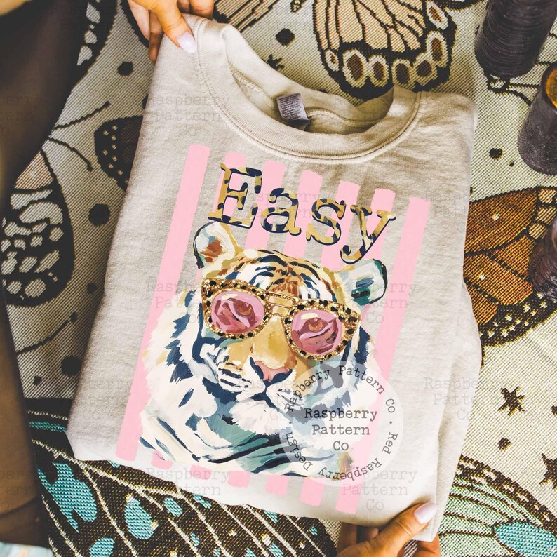 May include: A light gray sweatshirt featuring a tiger wearing pink sunglasses. The word "Easy" is printed above the tiger in a leopard print font, with pink vertical stripes behind the text and tiger.