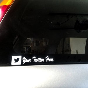 May include: A black car with a white sticker on the back window. The sticker has a Twitter bird logo and the text "Your Twitter Here".