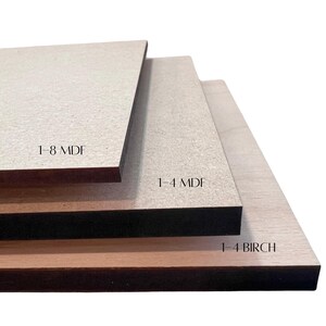 May include: Three rectangular wood boards of varying thicknesses are stacked. The top board is labeled "1-8 MDF", the middle board is labeled "1-4 MDF", and the bottom board is labeled "1-4 BIRCH". The boards are light brown and beige.