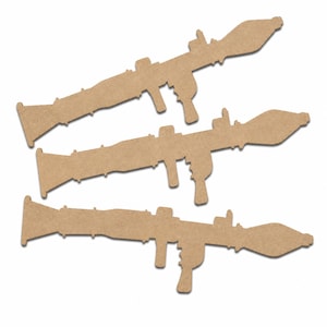May include: Three identical light brown, flat, laser-cut wooden shapes in the silhouette of a rocket-propelled grenade launcher. Each cutout features a long cylindrical tube, a flared rear exhaust, a pistol grip, and a front-mounted warhead.
