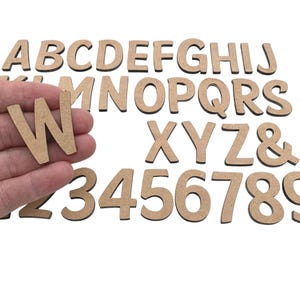Könnte beinhalten: Ein Satz aus Holzbuchstaben und -zahlen in hellbrauner Farbe. Die Buchstaben sind in Großbuchstaben und die Zahlen in einer Standardschriftart. Die Buchstaben und Zahlen sind in zufälliger Reihenfolge angeordnet.