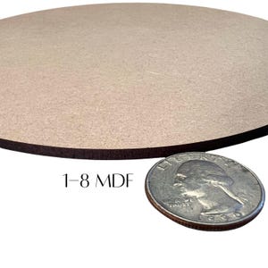 May include: A round, unfinished MDF wood piece with a dark brown edge. The text "1-8 MDF" is printed on the surface. A U.S. quarter coin is placed next to the wood piece for size comparison.