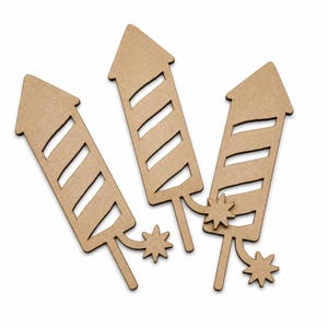 May include: Three wooden firework cutouts. Each firework is light brown with a pointed top and a series of diagonal cut-out lines. A starburst shape is at the bottom of each firework.
