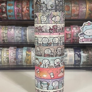 May include: A stack of ten washi tapes featuring a repeating pattern of cute cartoon characters with different expressions and activities. The tapes are all white with black outlines and feature various colors, including pink, blue, and yellow.