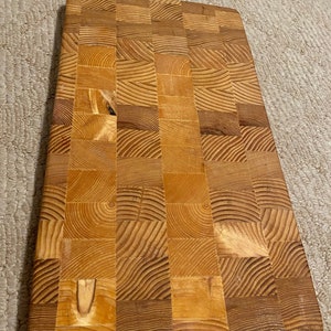 May include: A large, rectangular wooden cutting board with a checkered pattern. The board is made of light brown wood and has a natural finish.