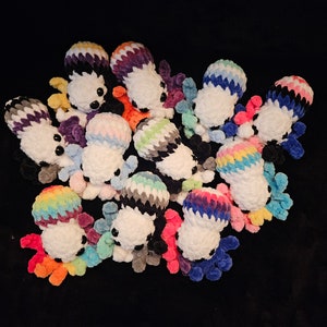 May include: A collection of crocheted octopus plushies in various colours, including rainbow, black and white, and gender pride colours. Each octopus has a white body and colourful tentacles.