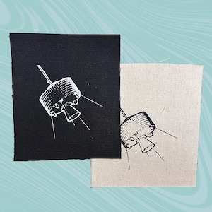 May include: Two fabric patches with a white outline of a satellite on a black and beige background.