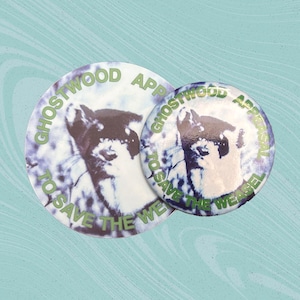 May include: Two circular badges featuring a weasel illustration. The badges have a white base with a purple and blue watercolour effect. The text "GHOSTWOOD APPEAL TO SAVE THE WEASEL" is printed in green around the edge of the badges.