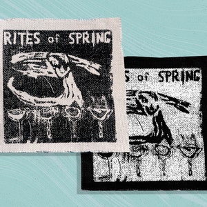 Peut inclure: Deux patchs en tissu noir et blanc avec le texte "Rites of Spring" et un design abstrait. Les patchs sont sur un fond bleu clair.