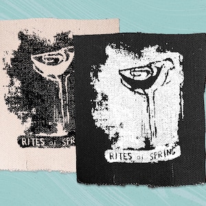 May include: Two fabric patches with a black and white image of a cocktail glass. The text "RITES of SPRING" is printed on both patches.