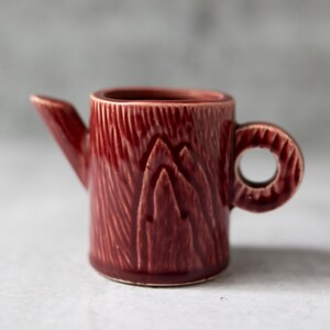 以下が含まれることがあります： 木の切り株の形をした、小さな赤い陶器のクリーマー。クリーマーにはハンドルと注ぎ口があります。