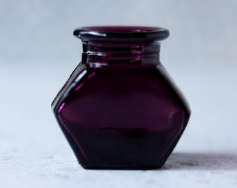 Tintero antiguo de vidrio morado con forma hexagonal.