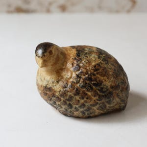 May include: A ceramic quail figurine with a speckled pattern in shades of brown, tan, and black. The bird has a rounded body and a small, detailed head. This decorative piece is suitable for home decor.