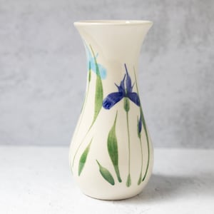 May include: A white ceramic vase with a pear-shaped body and a narrow neck. The vase is decorated with a blue and green floral pattern of irises.