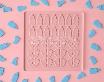 Puede incluir: Un molde de silicona rosa con 36 recortes para hacer decoraciones de fondant o pasta de goma en forma de biberón y pie de bebé. El molde está rodeado de chispas azules en forma de biberón y pie de bebé.