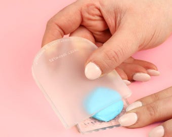 Puede incluir: Una espátula de silicona transparente con el texto "SWEET SPRING" y "DESIGNED IN ITALY" en ella. La espátula se está utilizando para alisar un fondant azul claro sobre una superficie texturizada.