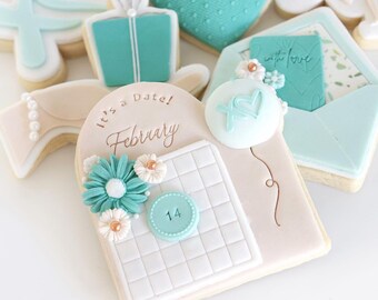 May include: A light pink and white cookie decorated with a calendar, flowers, and the text "It's a Date! February 14".