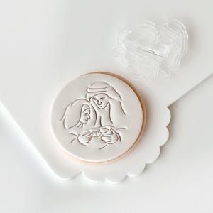 Op de afbeelding: Een witte koek met een reliëfdesign van een gezin met een baby. Het ontwerp is in een eenvoudige, minimalistische stijl.