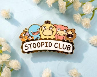 May include: A gold-toned metal enamel pin featuring five colorful cartoon creatures arranged in a row above a white banner with a scalloped black border that displays the black text STOOPID CLUB in a bold, sans-serif font.