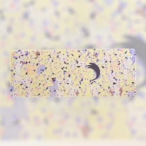 May include: A rectangular mousepad featuring a repeating pattern of yellow cartoon characters with black eyes and mouths. The background is a light yellow color. A black crescent moon shape is on the right side of the mousepad.