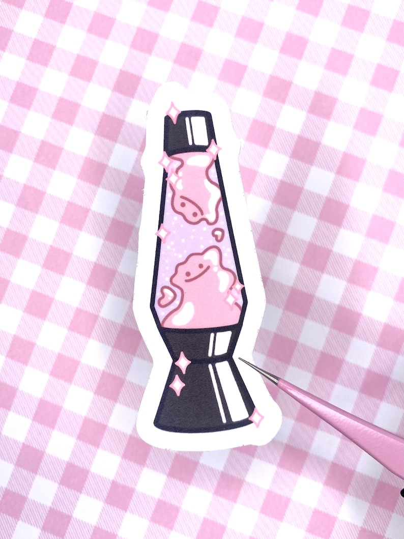 May include: A pink and white lava lamp sticker with a cute cartoon face and glitter. The sticker has a black base and a white outline.