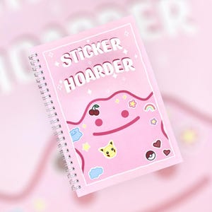 May include: Pink spiral bound notebook with the text "Sticker Hoarder" and a pink cartoon character with stickers on it.
