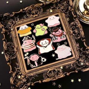 May include: A set of nine enamel pins featuring various Halloween-themed ghost characters. The pins are displayed in a gold ornate frame on a black background. The characters include a vampire, a mummy, a pirate, a ghost with a heart, a ghost with a cowboy hat, a ghost with a candy cane, and a ghost with a pumpkin.
