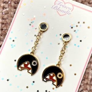 May include: A pair of gold-toned earrings featuring a black, cartoon-like design with a red and white mouth. The earrings are connected by a chain and have a circular top. The earrings are on a white card with the text "Frisco Blondie".