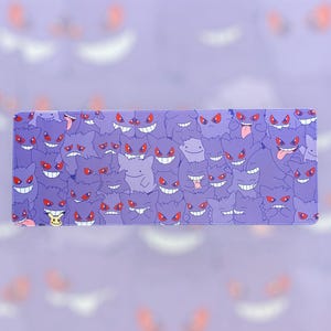 May include: A rectangular purple mousepad featuring a repeating pattern of cartoon ghosts with red eyes and wide smiles. A small yellow Pikachu character is also visible. The mousepad is designed for computer use.